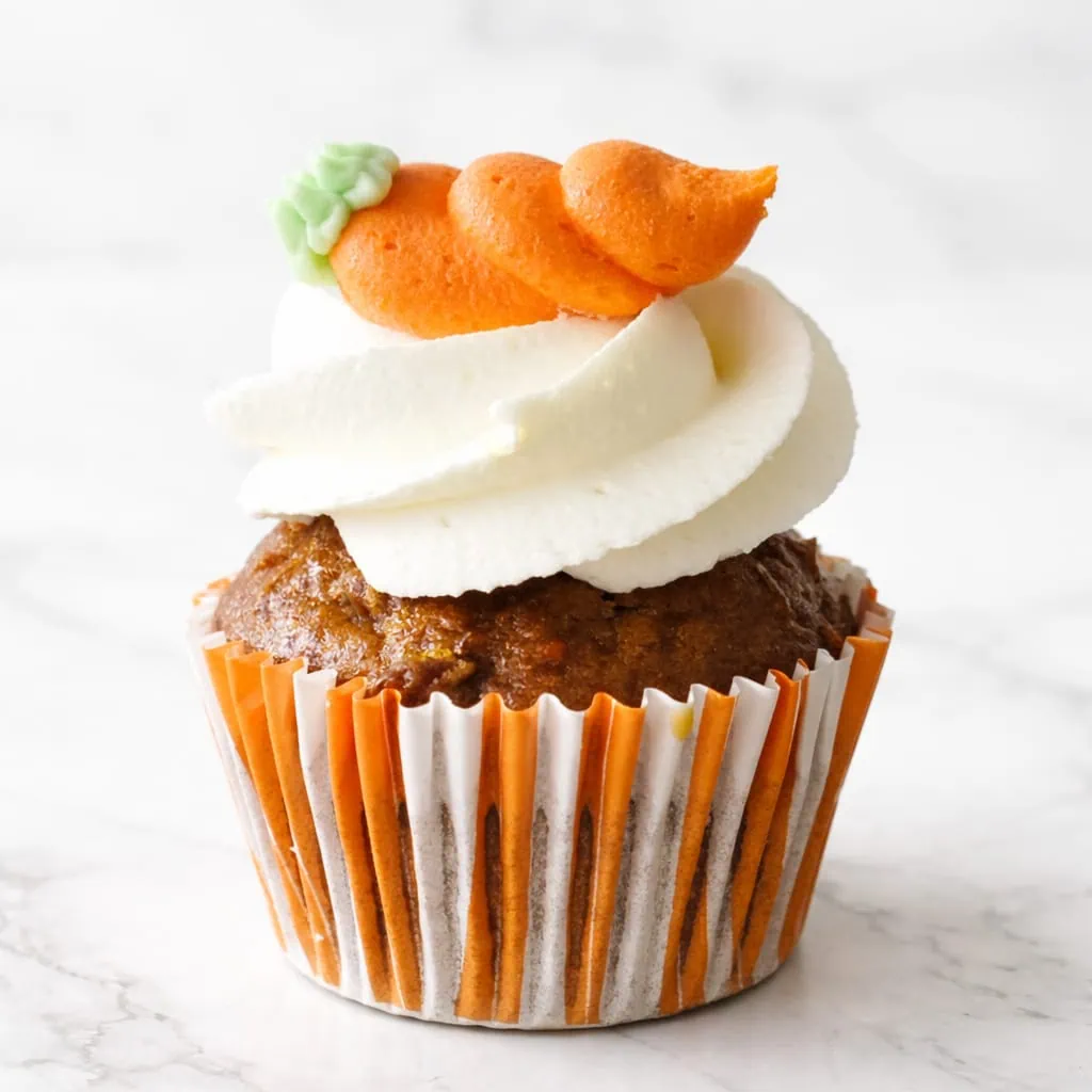 Moist carrot cupcake topped with smooth cream cheese frosting and a fondant carrot decoration.