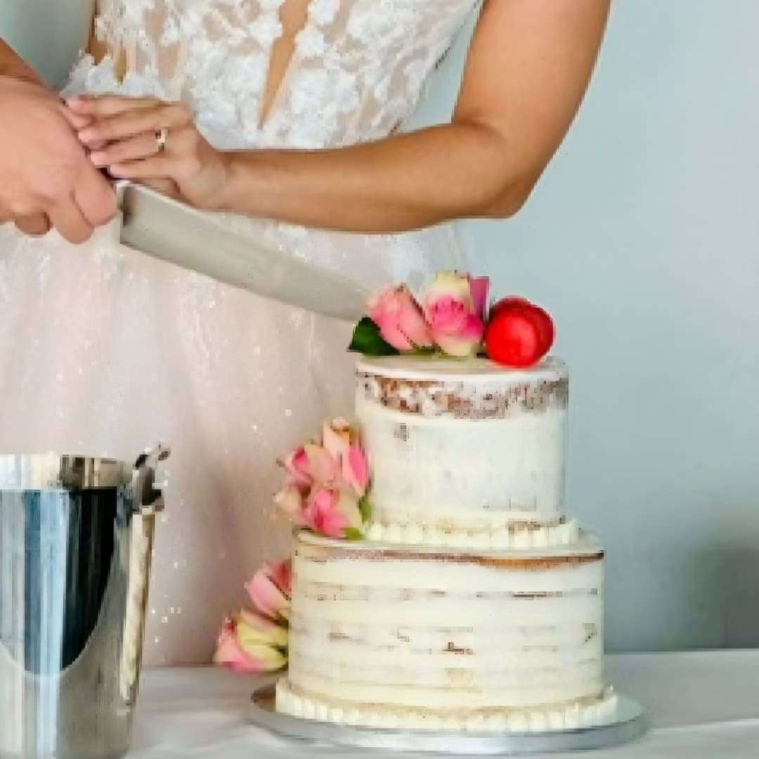 Two-tier semi-naked wedding cake adorned with pink macarons and delicate pink roses.