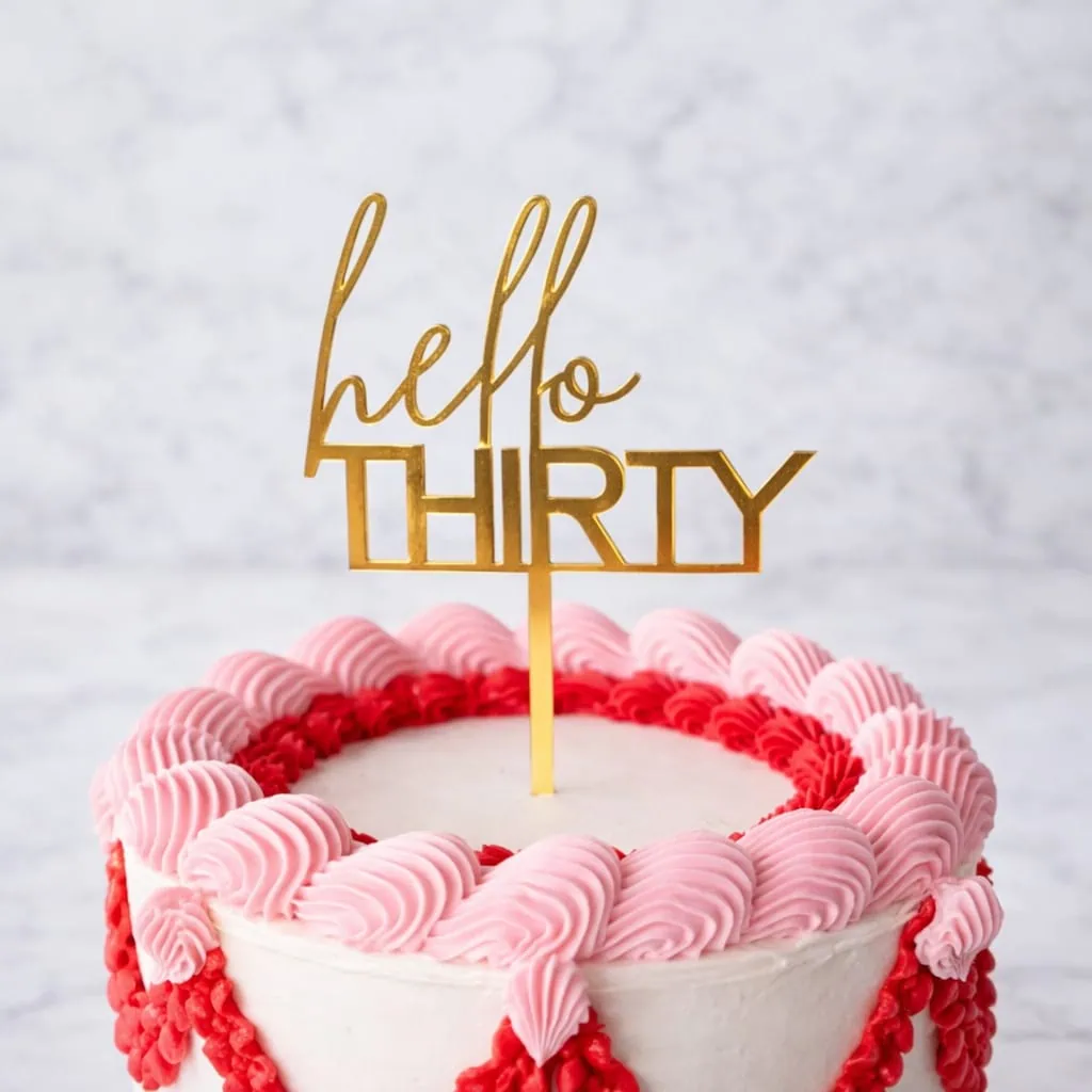 Gold "Hello Thirty" acrylic cake topper on birthday cake.