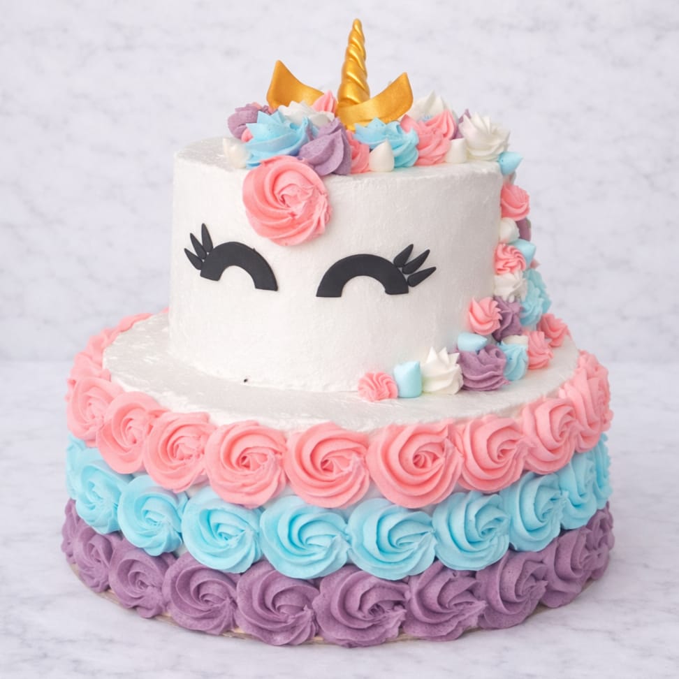 Unicorn Layer Cake with vanilla and rainbow tiers, decorated with buttercream rosettes and unicorn horn.