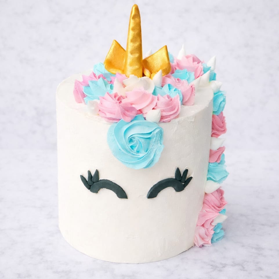 Unicorn Rainbow Layer Cake covered in white fondant with pastel-colored rosettes and a golden unicorn horn.
