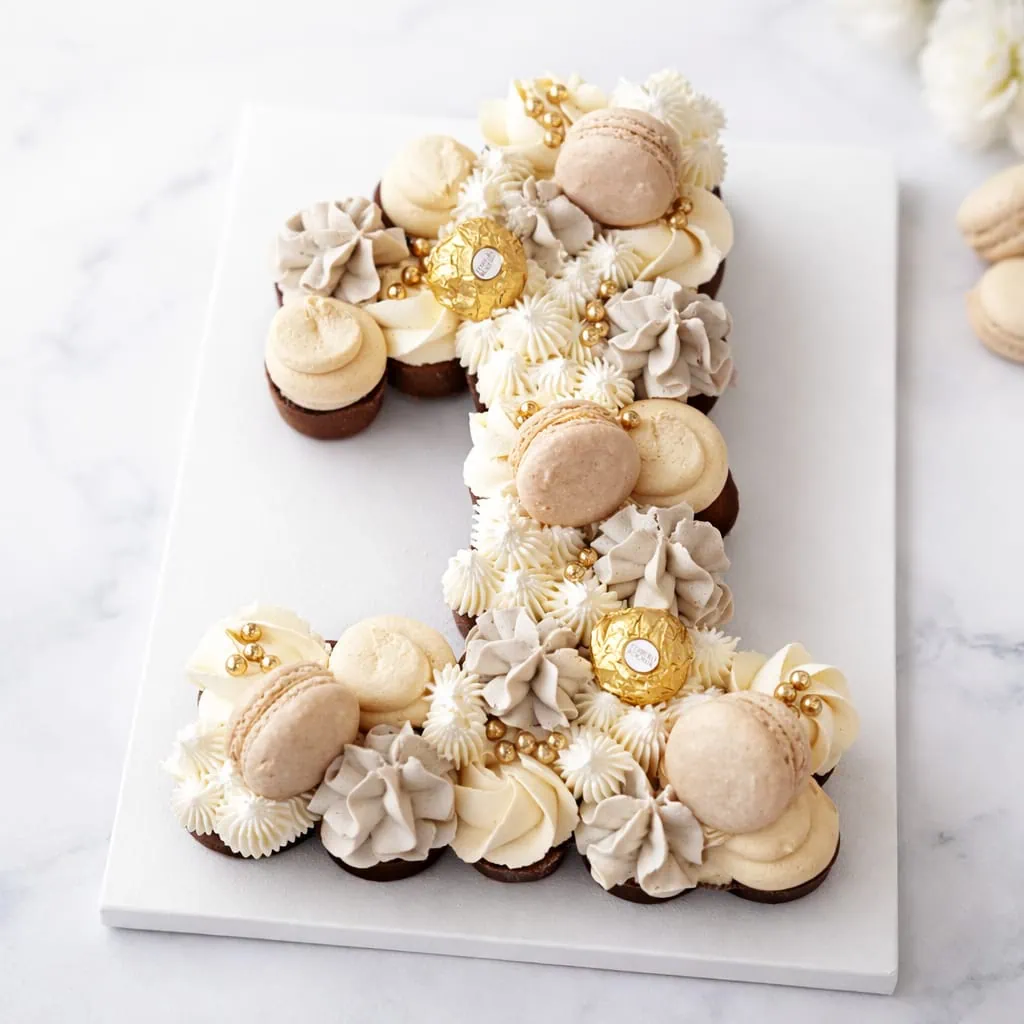 Luxury number cupcake cake made from mini cupcakes with macarons, buttercream and gold chocolate decoration.