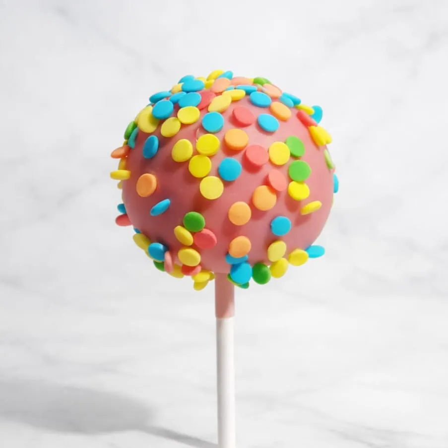 Pink cakepop dipped in pink chocolate and decorated with multicolored confetti sprinkles.